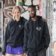 Lade das Bild in den Galerie-Viewer, Auf dem Bild sind 2 Models. Sie stehen vor bunten Wänden an der Gegengerade des Millerntor Stadions. Heimat des FC St. Pauli. Die Models tragen jeweils eine schwarze Kapuzenjacke. Die Ärmel sind dunkelgrau abgesetzt. Auf der linken Brustseite ist ein silbergraues 1910 Herz eingestickt.