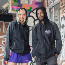 Lade das Bild in den Galerie-Viewer, Auf dem Bild sind 2 Models. Sie stehen vor bunten Wänden an der Gegengerade des Millerntor Stadions. Heimat des FC St. Pauli. Die Models tragen jeweils eine schwarze Kapuzenjacke. Die Ärmel sind dunkelgrau abgesetzt. Auf der linken Brustseite ist ein silbergraues 1910 Herz eingestickt.