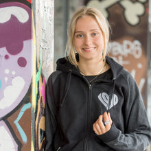 Lade das Bild in den Galerie-Viewer, Auf dem Bild ist 1 Model. Sie steht vor bunten Wänden an der Gegengerade des Millerntor Stadions. Heimat des FC St. Pauli. Das Model trägt eine schwarze Kapuzenjacke. Die Ärmel sind dunkelgrau abgesetzt. Auf der linken Brustseite ist ein silbergraues 1910 Herz eingestickt.