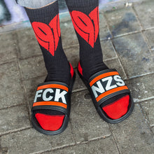 Lade das Bild in den Galerie-Viewer, Auf dem Foto sieht man 2 Füße eines Models. Das Model steht auf einem Steinboden und trägt schwarze Socken bei denen Fersen und Zehenbereich rot ist. Sowie vorne, mittig jeweils ein großes, rotes 1910 Herz eingestickt ist. Die Füße stecken in schwarz weiß roten Badelatschen. Auf den Badelatschen steht in Großbuchstaben FCK NZS.