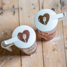 Lade das Bild in den Galerie-Viewer, Auf dem Bild sieht man einen Holzfußboden. Auf diesem stehen 2 Plastik Stadionbecher. Auf den Bechern befinden sich jeweils 1 weißer runder Becherdeckel. Auf diesen ist jeweils 1 braunes Herz und ein Flutlichtmast abgebildet.