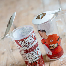 Lade das Bild in den Galerie-Viewer, Auf dem Bild sieht man einen Holzfußboden. Auf diesem stehen 2 bunte Plastik Stadionbecher. Auf den Bechern befinden sich jeweils 1 weißer runder Becherdeckel. Auf diesen ist jeweils 1 braunes Herz und ein Flutlichtmast abgebildet.