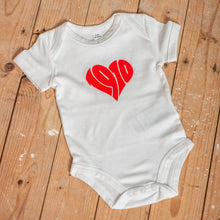 Lade das Bild in den Galerie-Viewer, Auf dem Bild sieht man einen Holzfußboden. Auf diesem liegt ein weißer Babybody mit rotem, herzförmigen Aufdruck 1910.