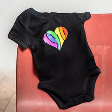 Lade das Bild in den Galerie-Viewer, Auf dem Bild hängt ein schwarzer Babybody mit regenbogenfarbenen 1910 Herz Aufdruck.