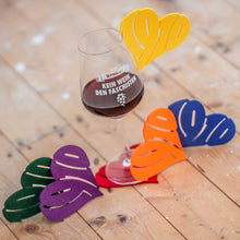 Lade das Bild in den Galerie-Viewer, Auf dem Foto sieht man einen Holzfußboden. Auf diesem befinden sich fünf Filzuntersetzer und ein Weinglas gefüllt mit Rotwein. Auf dem Glas befindet sich der Aufdruck 1910 Weinbar Kein Wein den Faschisten sowie eine Traube in Fußballoptik. Es hängt außerdem ein gelber Filzuntersetzer am Glasrand. Desweiteren liegen ein oranger, ein roter, ein lila, ein blauer und ein grüner Untersetzer um das Glas verteilt. Jeder Untersetzer ist herzförmig ausgestanzt und die Zahl 1910 zu erkennen.