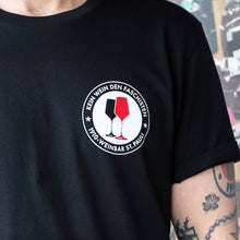 Lade das Bild in den Galerie-Viewer, Auf dem Bild sieht man eine Nahaufnahme eines schwarzen T Shirts. Auf diesem ist ein rundes Logo mit der Aufschrift Kein Wein den Faschisten, 1910 Weinbar St.Pauli sowie 2 Weingläser. Ein rotes und ein schwarzes. In Anlehnung an das klassische Antifa Logo.