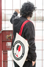 Lade das Bild in den Galerie-Viewer, Auf dem Bild sieht man ein Model angelehnt an ein Gitter. Über der rechten Schulter trägt er einen naturfarbenen Jutebeutel mit roten Henkeln. Auf der Tasche befindet sich der Aufdruck Kein Wein den Faschisten sowie 1910 Weinbar St.Pauli und einem schwarzen und einem roten Weinglas. In Anlehnung an das klassische Antifa Logo.