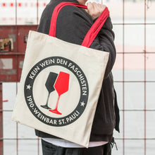 Lade das Bild in den Galerie-Viewer, Auf dem Bild sieht man einen naturfarbenen Jutebeutel mit roten Henkeln. Auf der Tasche befindet sich der Aufdruck Kein Wein den Faschisten sowie 1910 Weinbar St.Pauli und einem schwarzen und einem roten Weinglas. In Anlehnung an das klassische Antifa Logo.