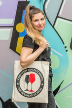 Lade das Bild in den Galerie-Viewer, Auf dem Bild sieht man ein Model vor einer bunten Wand. Über der rechten Schulter trägt sie einen naturfarbenen Jutebeutel mit schwarzen Henkeln. Auf der Tasche befindet sich der Aufdruck Kein Wein den Faschisten sowie 1910 Weinbar St.Pauli und einem schwarzen und einem roten Weinglas. In Anlehnung an das klassische Antifa Logo.