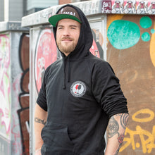 Lade das Bild in den Galerie-Viewer, Ihr seht auf dem Bild 1 Model vor einer bunten Wand. Er trägt einen schwarzen Kapuzenpulli mit dem Pocketprint Kein Wein den Faschisten sowie 1910 Weinbar St.Pauli und einem roten und einem schwarzen Weinglas. In Anlehnung an das klassische Antifa Logo. Das Foto entstand vor dem Millerntor Stadion. Heimat des FC St.Pauli.