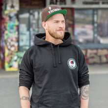 Lade das Bild in den Galerie-Viewer, Ihr seht auf dem Bild 1 Model vor einer bunten Wand. Er trägt einen schwarzen Kapuzenpulli mit dem Pocketprint Kein Wein den Faschisten sowie 1910 Weinbar St.Pauli und einem roten und einem schwarzen Weinglas. In Anlehnung an das klassische Antifa Logo. Das Foto entstand vor der Gegengerade des Millerntor Stadions. Heimat des FC St.Pauli.