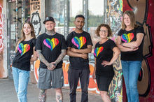 Lade das Bild in den Galerie-Viewer, Auf dem Foto sieht man fünf Models. Sie stehen nebeneinander vor einer bunten Wand. Alle tragen schwarze Shirts mit jeweils einem großen 1910 Herz Druck in regenbogenfarben. Das Foto entstand vor dem Millerntor Stadion. Heimat des FC St.Pauli.