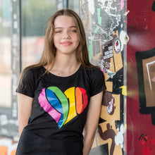 Lade das Bild in den Galerie-Viewer, Auf dem Foto sieht man ein Model an eine bunte Wand gelehnt. Sie trägt ein schwarzes tailliertes Shirt. Auf dem Shirt ist ein großes 1910 Herz in regenbogenfarben gedruckt. Das Foto entstand vor dem Millerntor Stadion. Heimat des FC St.Pauli.