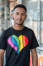 Lade das Bild in den Galerie-Viewer, Auf dem Bild sieht man ein Model in schwarzem T Shirt mit einem großen 1910 Herz Druck in regenbogenfarben. Das Model steht vor einer bunten Wand. Das Foto entstand vor dem Millerntor Stadion. Heimat des FC St.Pauli.