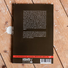 Lade das Bild in den Galerie-Viewer, Auf dem Foto sieht man einen Holzfußboden auf dem ein Buch liegt. Es handelt sich um die Rückseite eines Buches. Es ist dunkelbraun und es steht ein kurzer Text darauf in weißen Buchstaben. Unten befindet sich das 1910 e.V. Logo sowie ein EAN Code.