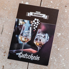 Lade das Bild in den Galerie-Viewer, Auf dem Bild sieht man einen Holzfußboden. Auf diesem liegt ein Gutschein für die 1910 Weinbar. Es sind 2 Weingläser abgebildet auf denen der Schriftzug Kein Wein den Faschisten zu sehen ist.