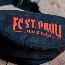 Lade das Bild in den Galerie-Viewer, Auf dem Bild sieht man eine Nahaufnahme einer schwarzen Gürteltasche. FC St. Pauli Museum ist in rot darauf eingestickt.
