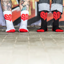 Lade das Bild in den Galerie-Viewer, Auf dem Foto sieht man die Füße zweier Models. Das linke Model trägt weiße Socken mit roten Zehen und Fersenbereich sowie jeweils einem großen, roten 1910 Herz mittig eingestickt.  Das rechte Model trägt schwarze Socken. Diese haben auch rote Fersen und Zehenbereiche sowie jeweils ein großes rotes 1910 Herz mittig eingestickt. Sie stehen nebeneinander auf einem Steinfußboden vor einer bunten Wand. Das Foto entstand vor dem Millerntor Stadion. Heimat des FC St.Pauli.
