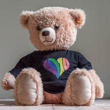 Lade das Bild in den Galerie-Viewer, Auf dem Bild sieht man einen hellbraunen Teddybären. Dieser trägt einen schwarzen Babybody mit einem regenbogenfarbenen 1910 Herz Aufdruck.

