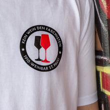 Lade das Bild in den Galerie-Viewer, Auf dem Bild sieht man eine Nahaufnahme eines weißen Shirts mit dem Pocketprint Kein Wein den Faschisten sowie 1910 Weinbar St.Pauli und einem schwarzen und einem roten Weinglas. In Anlehnung an das klassische Antifa Logo.
