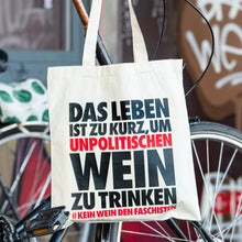 Lade das Bild in den Galerie-Viewer, Auf dem Bild sieht man einen naturfarbenen Jutebeutel der über einem Fahrrad hängt. Auf dem Beutel befindet sich der Aufdruck Das Leben ist zu kurz um unpolitischen Wein zu trinken. Kein Wein den Faschisten.
