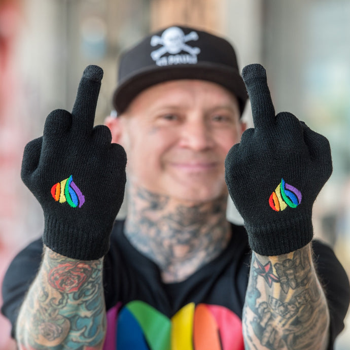 Auf dem Foto sieht man ein Model das mit beiden Händen den Mittelfinger in die Kamera hält. Die Hände stecken in schwarzen Handschuhen. Auf den Handschuhen ist jeweils ein 1910 Herz in regenbogenfarben aufgestickt.