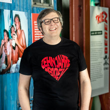 Lade das Bild in den Galerie-Viewer, Auf dem Foto sieht man ein Model vor einer blauen Wand. Er trägt ein schwarzes T Shirt mit einem großen, roten Aufdruck Zehn Jahre 1910 eV. Der Aufdruck ist herzförmig. Das Foto entstand im FC St.Pauli Museum.
