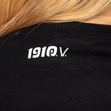 Lade das Bild in den Galerie-Viewer, Auf dem Foto sieht man eine Nahaufnahme eines Shirts. Es steht in weißen Buchstaben 1910 eV auf Nackenhöhe eines schwarzen Shirts.
