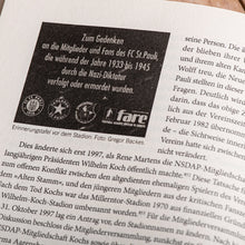 Lade das Bild in den Galerie-Viewer, Auf dem Bild sieht man eine Nahaufnahme einer Seite eines aufgeschlagenen Buches. Auf dieser Seite befindet sich ein dunkel hinterlegter Kasten mit dem Schriftzug Zum Gedenken an die Mitglieder und Fans des FC St.Pauli die während der Jahre 1933 bis 1945 durch die Nazi Diktatur verfolgt oder ermordet wurden.

