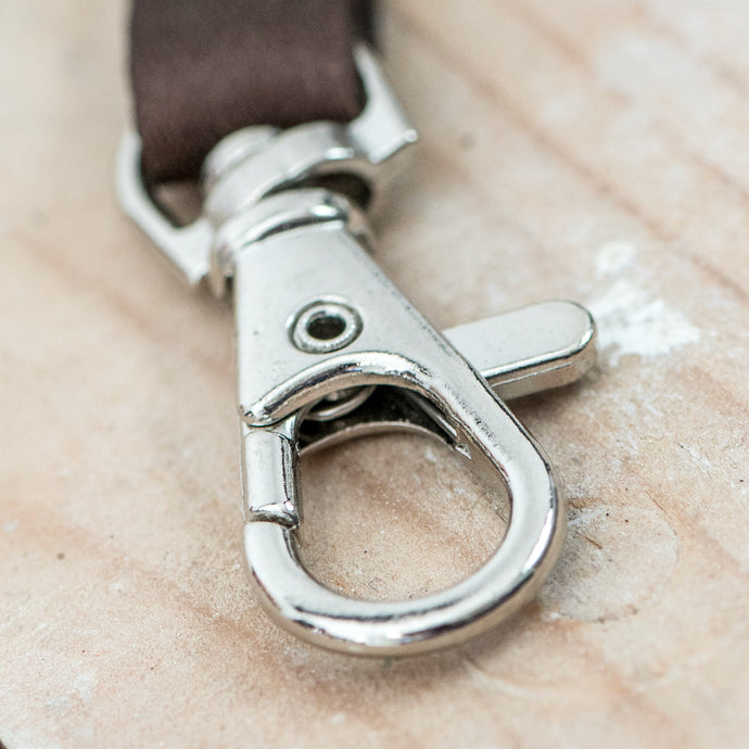 Auf dem Bild sieht man einen Holzboden. Auf diesem liegt ein kleiner Karabiner mit braunem Band.