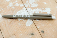 Lade das Bild in den Galerie-Viewer, Auf dem Bild sieht man einen Holzfußboden. Auf diesem liegt ein brauner Kugelschreiber. Auf dem Kugelschreiber ist in weiß gedruckt Museum für den FC St.Pauli sowie www.1910-museum.de

